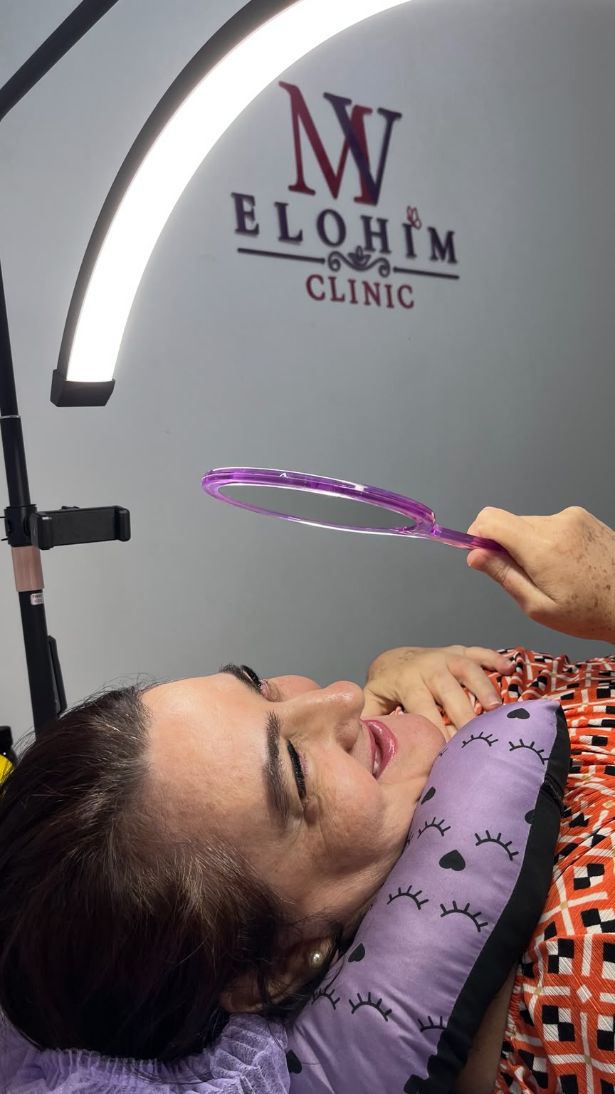 Cliente deitada na maca da Elohim Clinic observando o resultado do procedimento em um espelho de mão