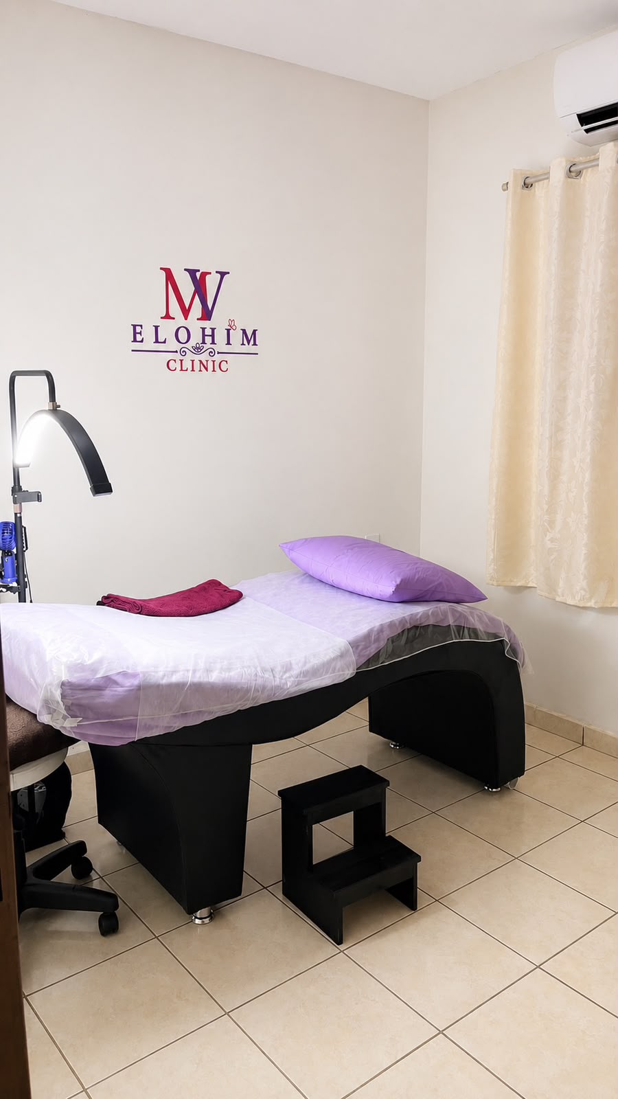 Sala de atendimento da Elohim Clinic com maca, apoio de degraus, iluminação profissional e a marca na parede